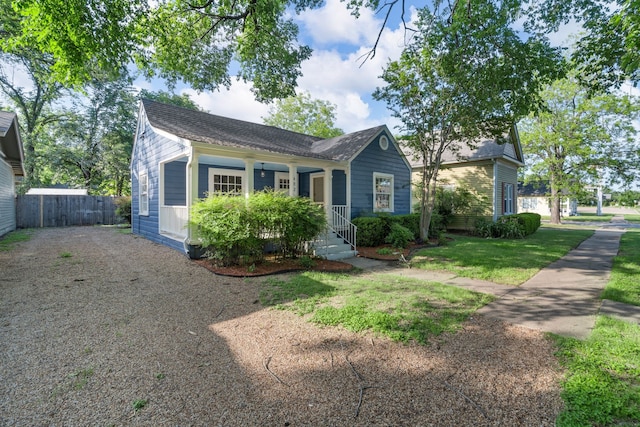 view of front of house with a front lawn, roof with shingles, fence, and gravel driveway