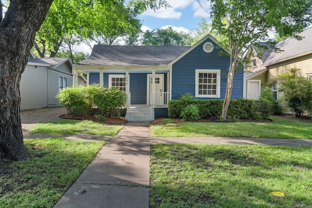view of front of house featuring roof with shingles, covered porch, and a front yard