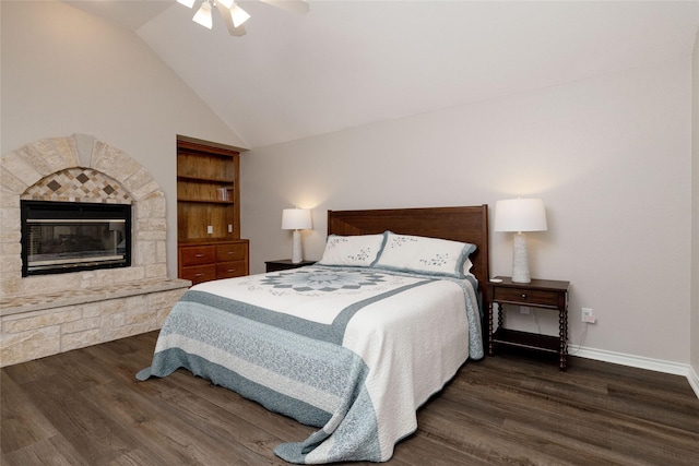bedroom featuring wood finished floors, baseboards, a stone fireplace, ceiling fan, and vaulted ceiling