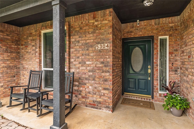 property entrance featuring covered porch and brick siding