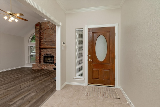 entryway with ceiling fan, a fireplace, light wood-style floors, baseboards, and ornamental molding