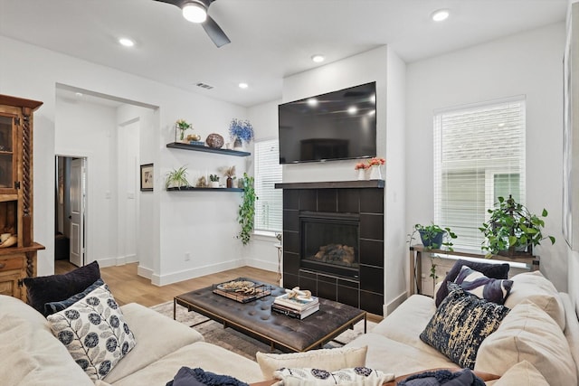 living room with a ceiling fan, visible vents, a tiled fireplace, wood finished floors, and baseboards