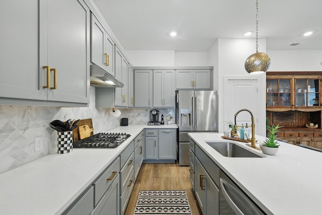 kitchen with light countertops, gray cabinets, under cabinet range hood, a sink, and appliances with stainless steel finishes