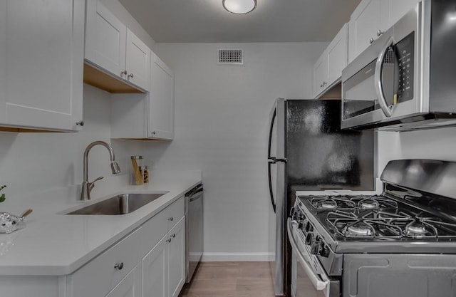 kitchen with a sink, light wood finished floors, stainless steel appliances, white cabinetry, and visible vents