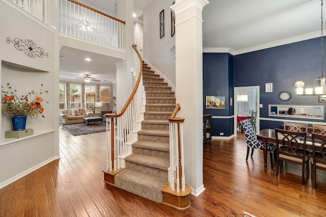 staircase with baseboards, a high ceiling, ceiling fan, and hardwood / wood-style floors