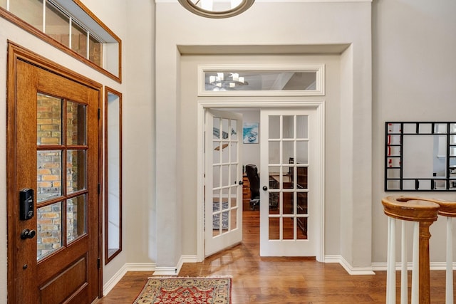 doorway featuring baseboards, french doors, wood finished floors, and a notable chandelier