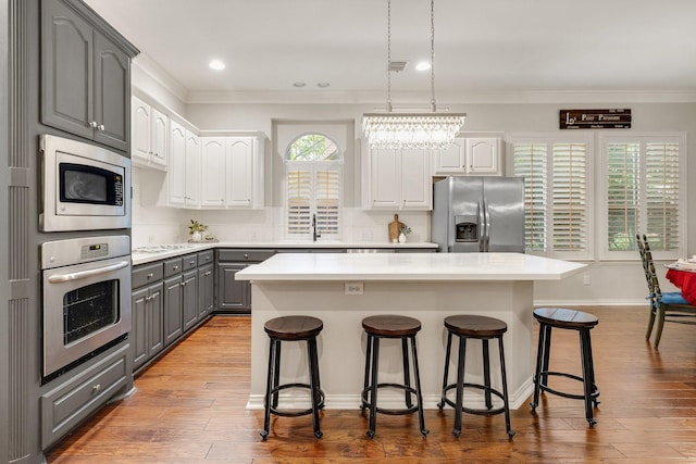 kitchen with gray cabinets, a kitchen island, crown molding, appliances with stainless steel finishes, and a breakfast bar