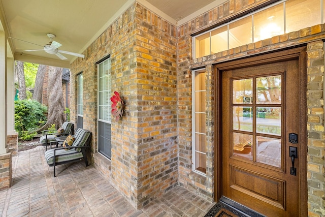 entrance to property featuring ceiling fan, a porch, and brick siding