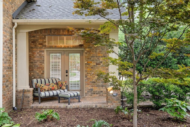 view of exterior entry with a shingled roof and brick siding
