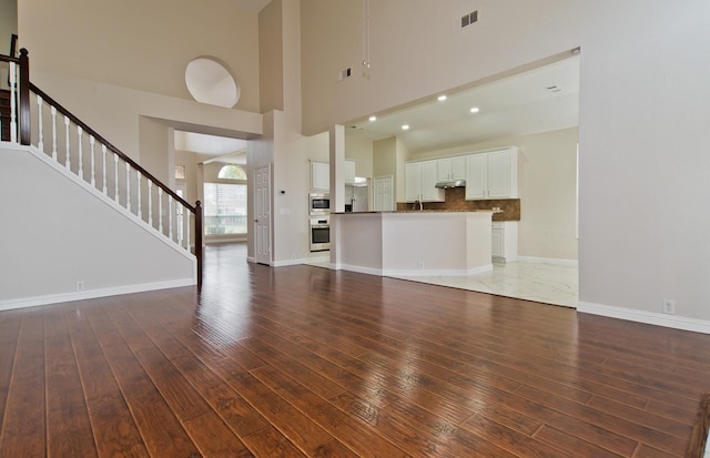 unfurnished living room with wood-type flooring, a high ceiling, baseboards, and stairs