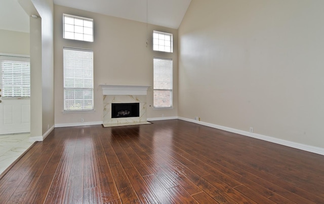 unfurnished living room featuring baseboards, high vaulted ceiling, a high end fireplace, and hardwood / wood-style floors