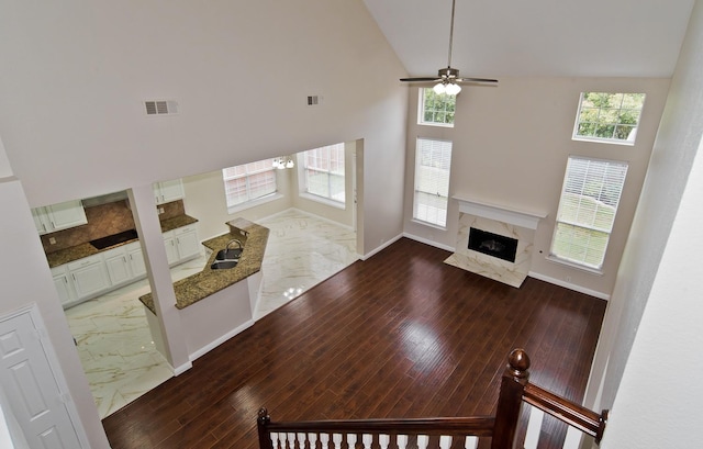 unfurnished living room featuring ceiling fan, visible vents, a high end fireplace, a sink, and high vaulted ceiling