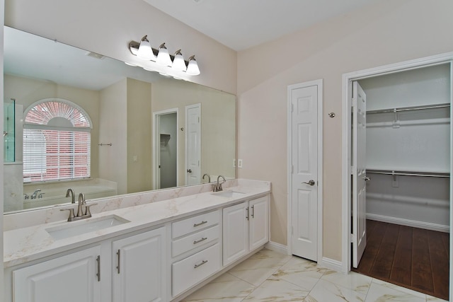 bathroom featuring a sink, baseboards, double vanity, and a spacious closet