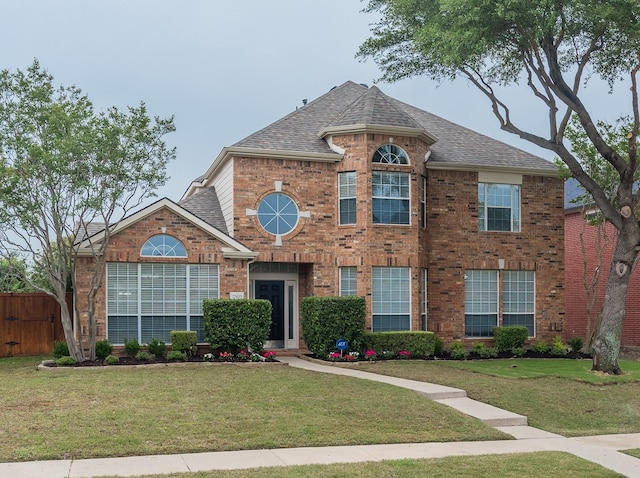 view of front of house with roof with shingles, fence, a front yard, and brick siding