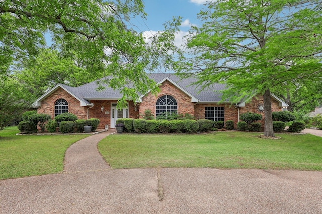 single story home featuring brick siding, a shingled roof, and a front yard