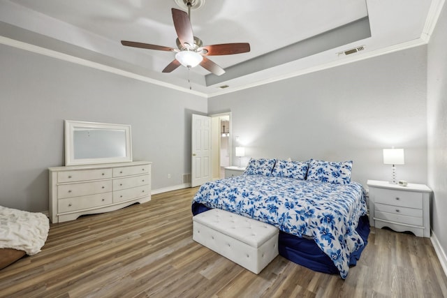 bedroom featuring visible vents, ornamental molding, wood finished floors, a raised ceiling, and a ceiling fan