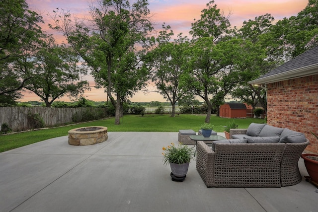 patio terrace at dusk with an outdoor structure, an outdoor living space with a fire pit, a fenced backyard, a shed, and a lawn