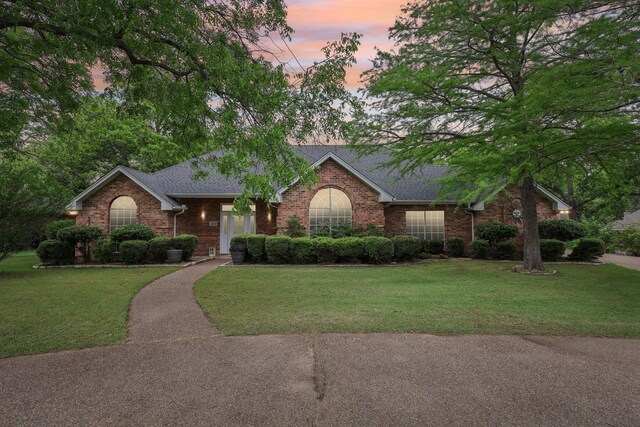 ranch-style home with a lawn, a shingled roof, and brick siding