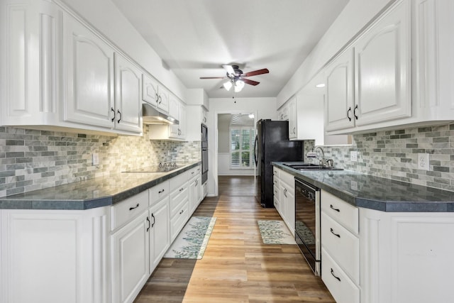 kitchen featuring ceiling fan, dark countertops, a sink, under cabinet range hood, and black appliances