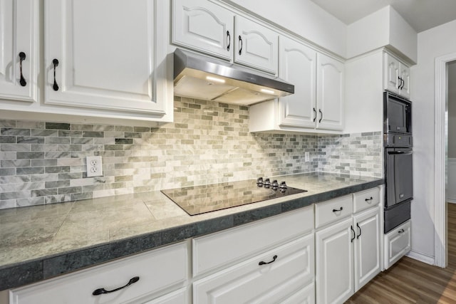 kitchen with dark wood finished floors, white cabinetry, tile countertops, under cabinet range hood, and black appliances