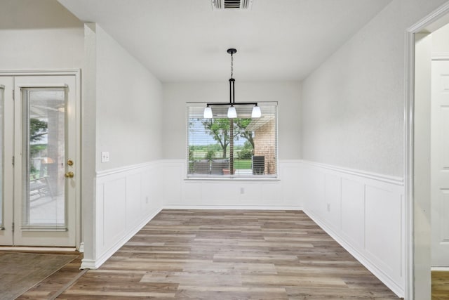 unfurnished dining area featuring visible vents, light wood-style flooring, and wainscoting