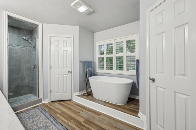bathroom featuring visible vents, a freestanding tub, a shower stall, wood finished floors, and baseboards