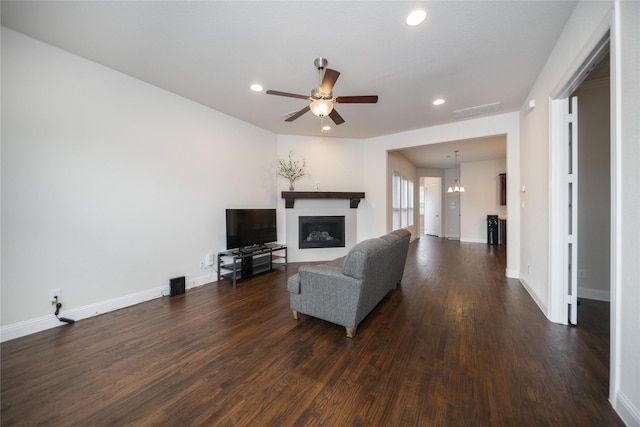 living room with recessed lighting, a glass covered fireplace, dark wood finished floors, and ceiling fan with notable chandelier