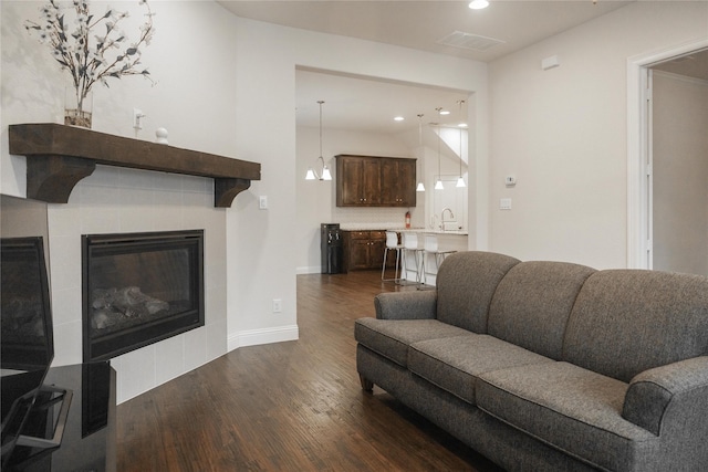 living area featuring visible vents, baseboards, dark wood-type flooring, recessed lighting, and a tile fireplace