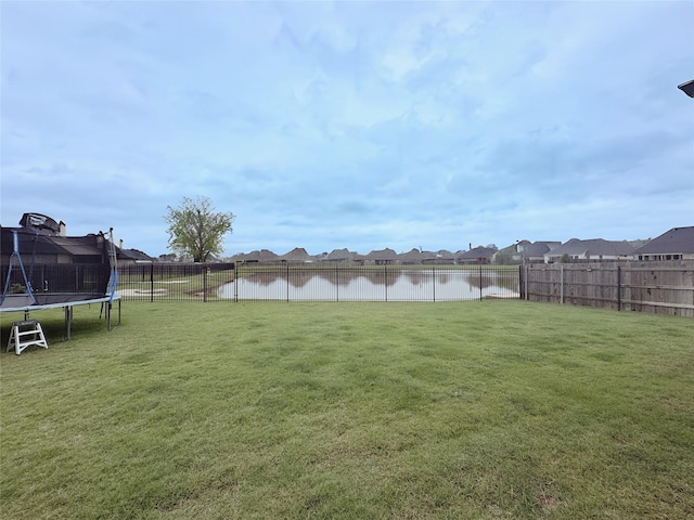 view of yard with a residential view, a trampoline, a water view, and a fenced backyard