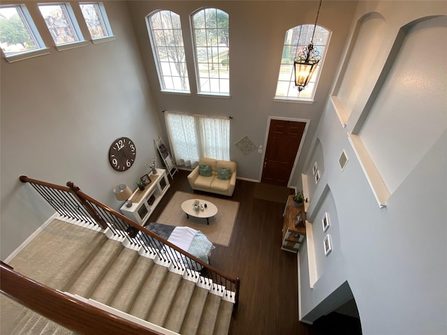living room with a towering ceiling, wood finished floors, baseboards, a notable chandelier, and stairs
