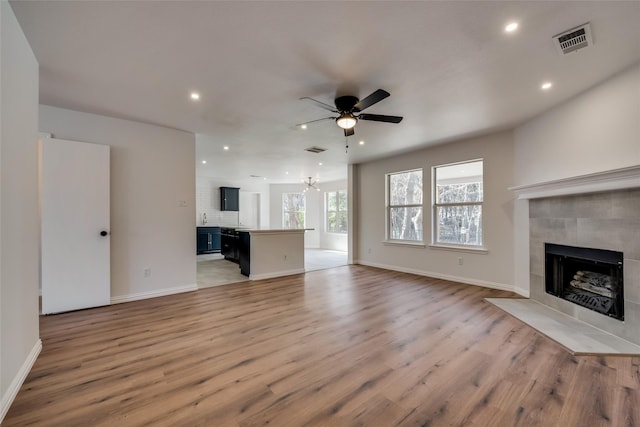 unfurnished living room with a fireplace, ceiling fan with notable chandelier, light wood-style flooring, and visible vents