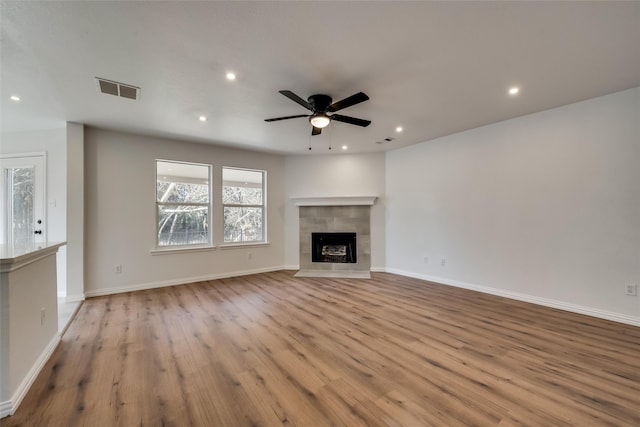 unfurnished living room with a ceiling fan, visible vents, a tiled fireplace, wood finished floors, and recessed lighting
