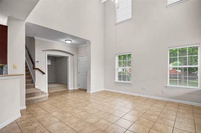 interior space with arched walkways, light tile patterned floors, stairway, ornamental molding, and a high ceiling