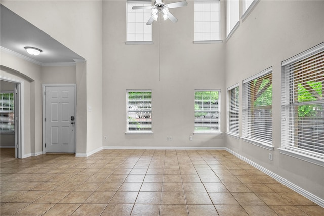 interior space with ceiling fan, crown molding, baseboards, a high ceiling, and light tile patterned flooring