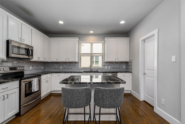 kitchen featuring a kitchen island, a kitchen bar, tasteful backsplash, a sink, and stainless steel appliances