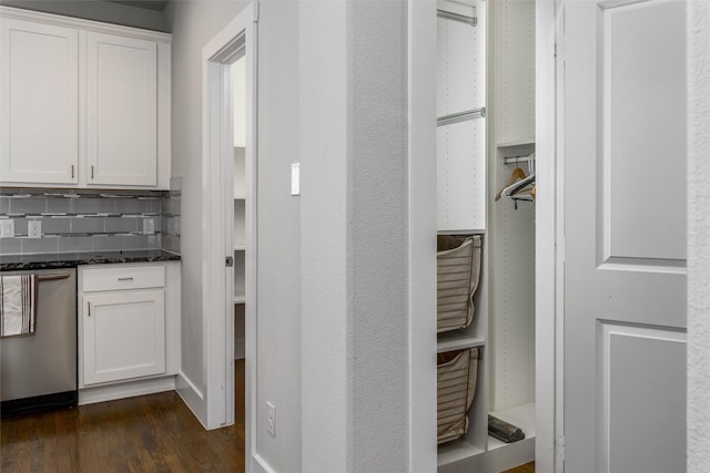 interior space featuring dark wood-style flooring, dark stone counters, white cabinetry, backsplash, and stainless steel dishwasher