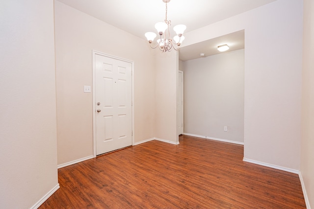 spare room with baseboards, an inviting chandelier, and wood finished floors