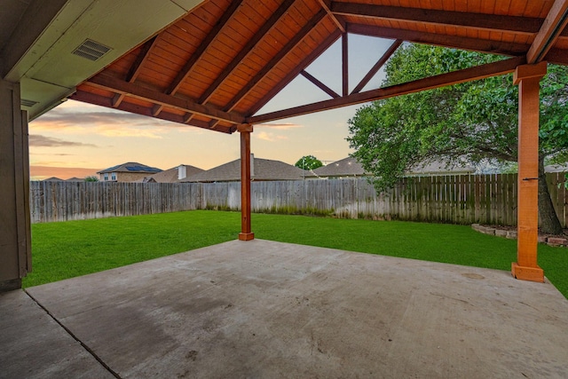 patio terrace at dusk with a lawn, a fenced backyard, and visible vents