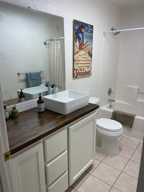 bathroom with tile patterned flooring, vanity, a textured wall, toilet, and shower / bath combo