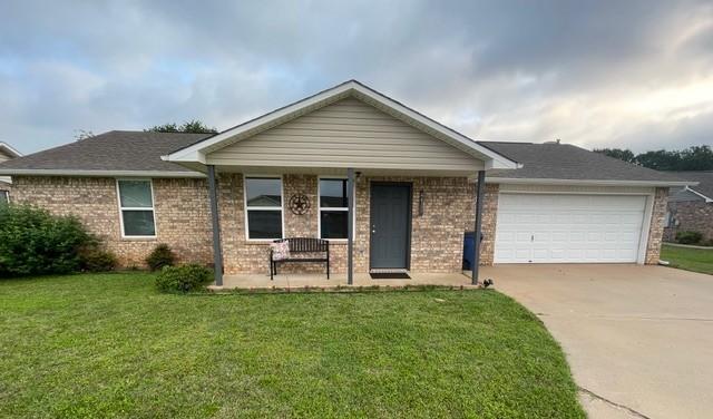 ranch-style house with covered porch, a front yard, a garage, brick siding, and concrete driveway