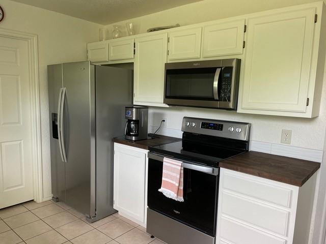 kitchen with wood counters, light tile patterned floors, white cabinets, and stainless steel appliances