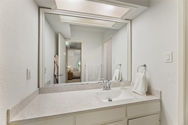 ensuite bathroom featuring connected bathroom, a textured wall, and vanity