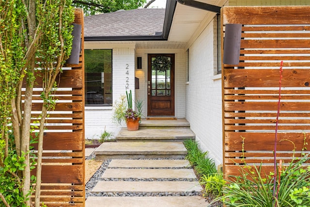 view of exterior entry featuring roof with shingles and brick siding