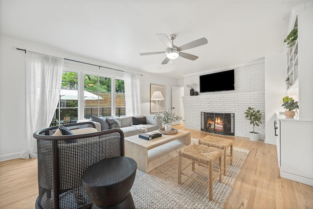 living area with ceiling fan, a brick fireplace, and light wood finished floors