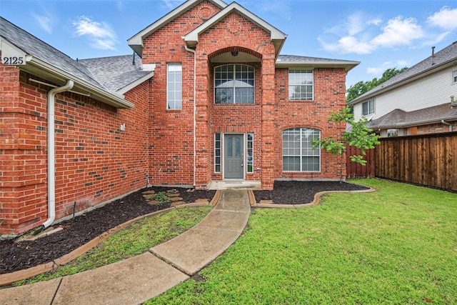 rear view of property with a yard, brick siding, fence, and roof with shingles
