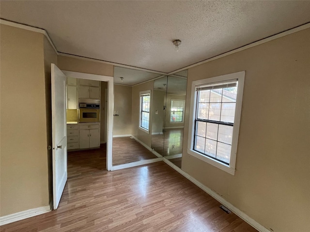 interior space with baseboards, ornamental molding, a textured ceiling, and light wood-type flooring
