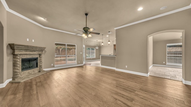 unfurnished living room featuring a ceiling fan, a fireplace, baseboards, arched walkways, and light wood-style flooring