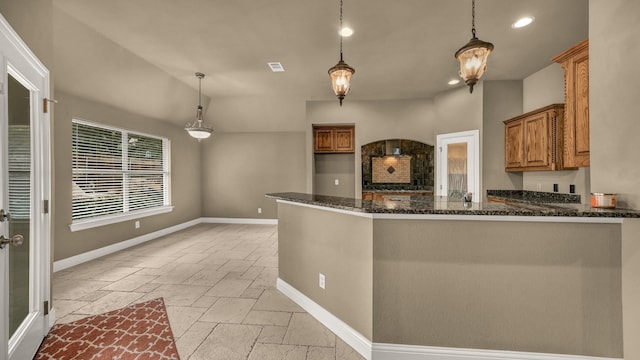 kitchen with hanging light fixtures, brown cabinets, dark stone counters, recessed lighting, and stone tile floors
