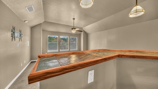 interior space with ceiling fan, carpet floors, baseboards, lofted ceiling, and visible vents