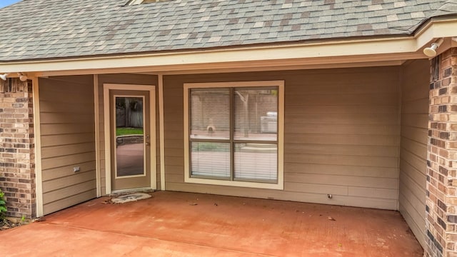 property entrance featuring a shingled roof and brick siding
